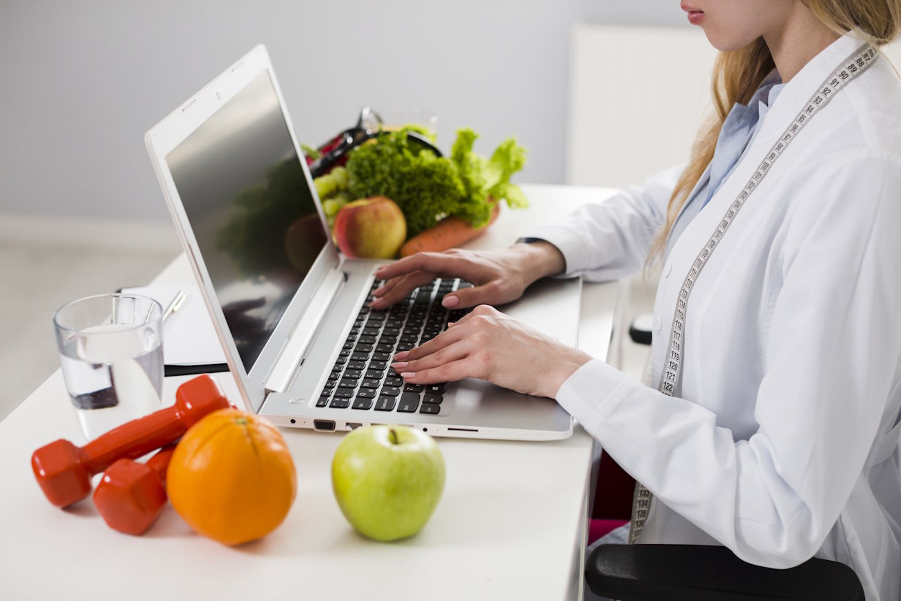 Imagem mostra mulher com computador e frutas à mesa, para simular como abrir CNPJ para nutricionista